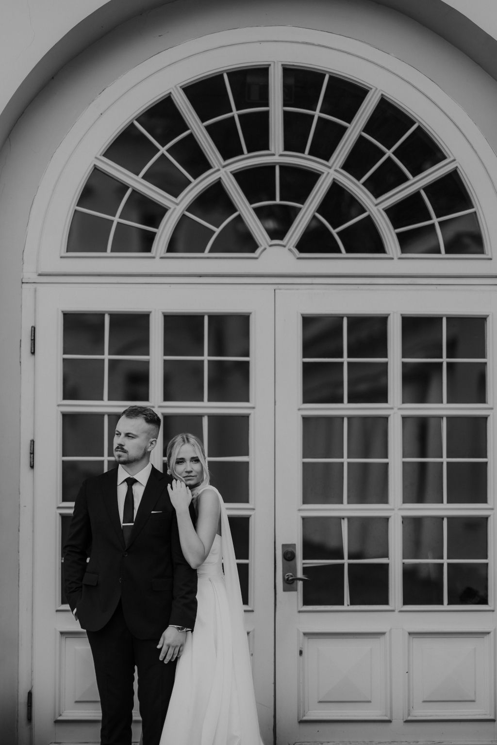 Wedding portrait in front of grand arched windows with architectural details.