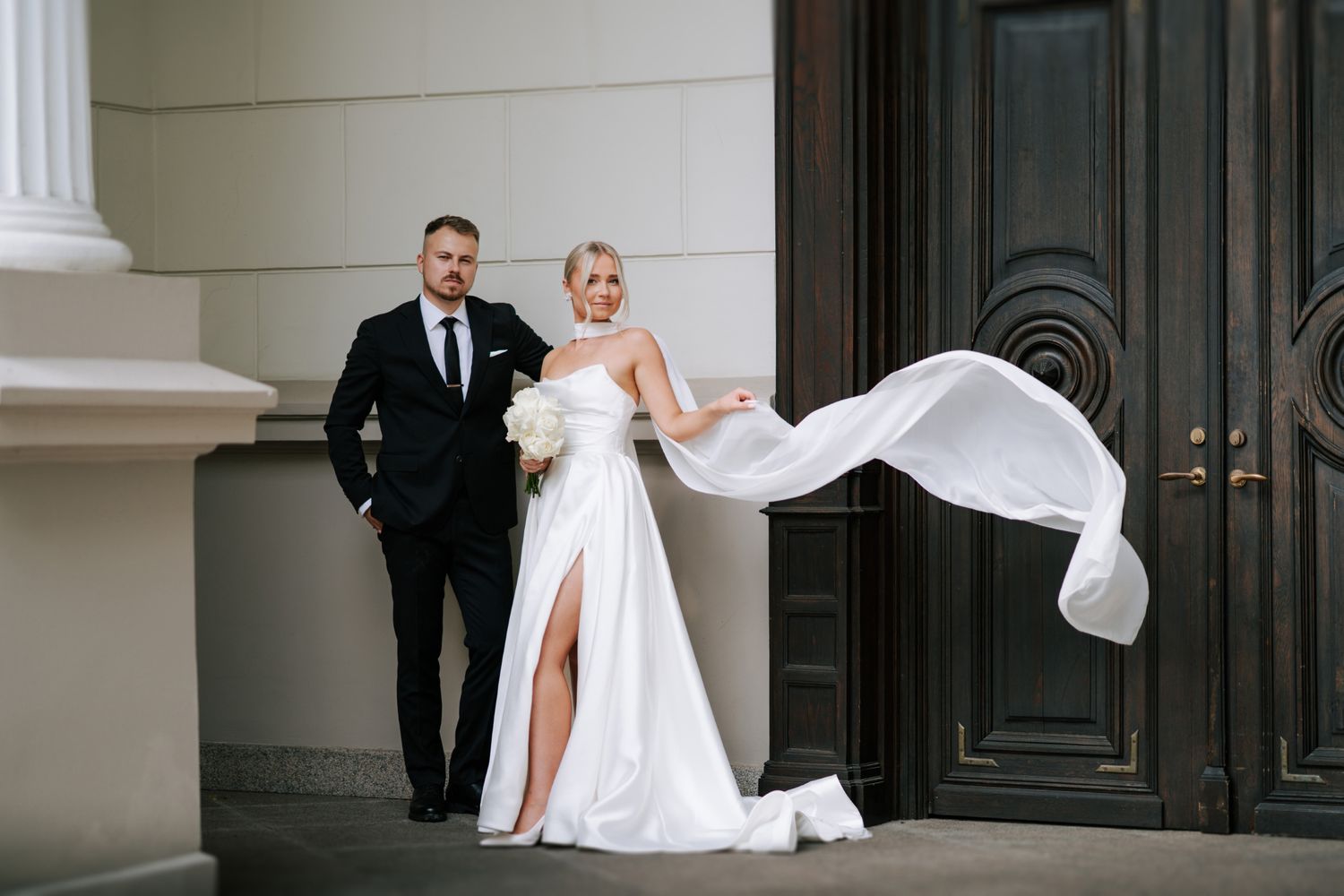 Elegant wedding couple posing in front of classic white architectural details.