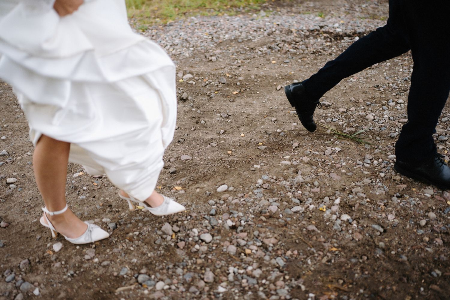 Wedding shoes and dress hem walking on a gravel path in an outdoor setting.