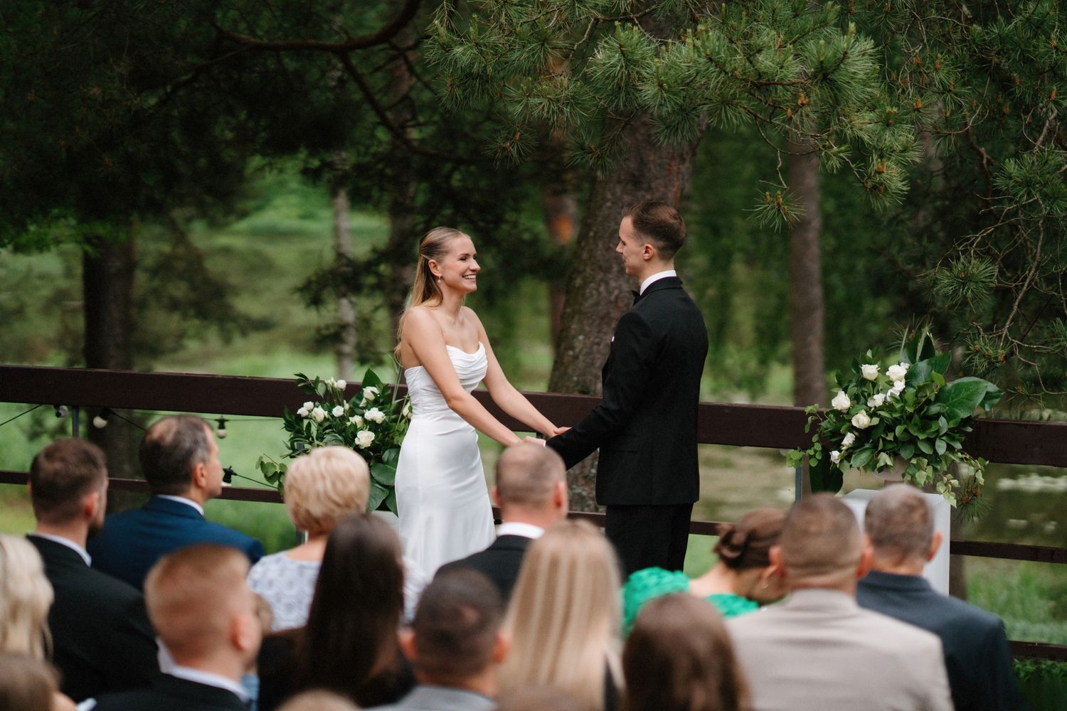 Wedding ceremony taking place in a lush green forest setting with guests watching.