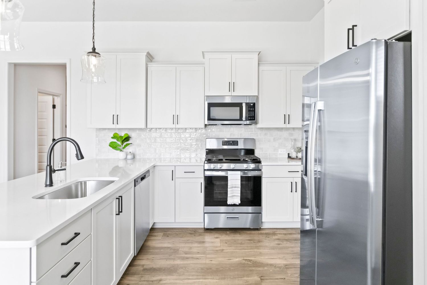 Modern white kitchen with shaker cabinets, quartz countertops, stainless appliances and hardwood floors in contemporary design.