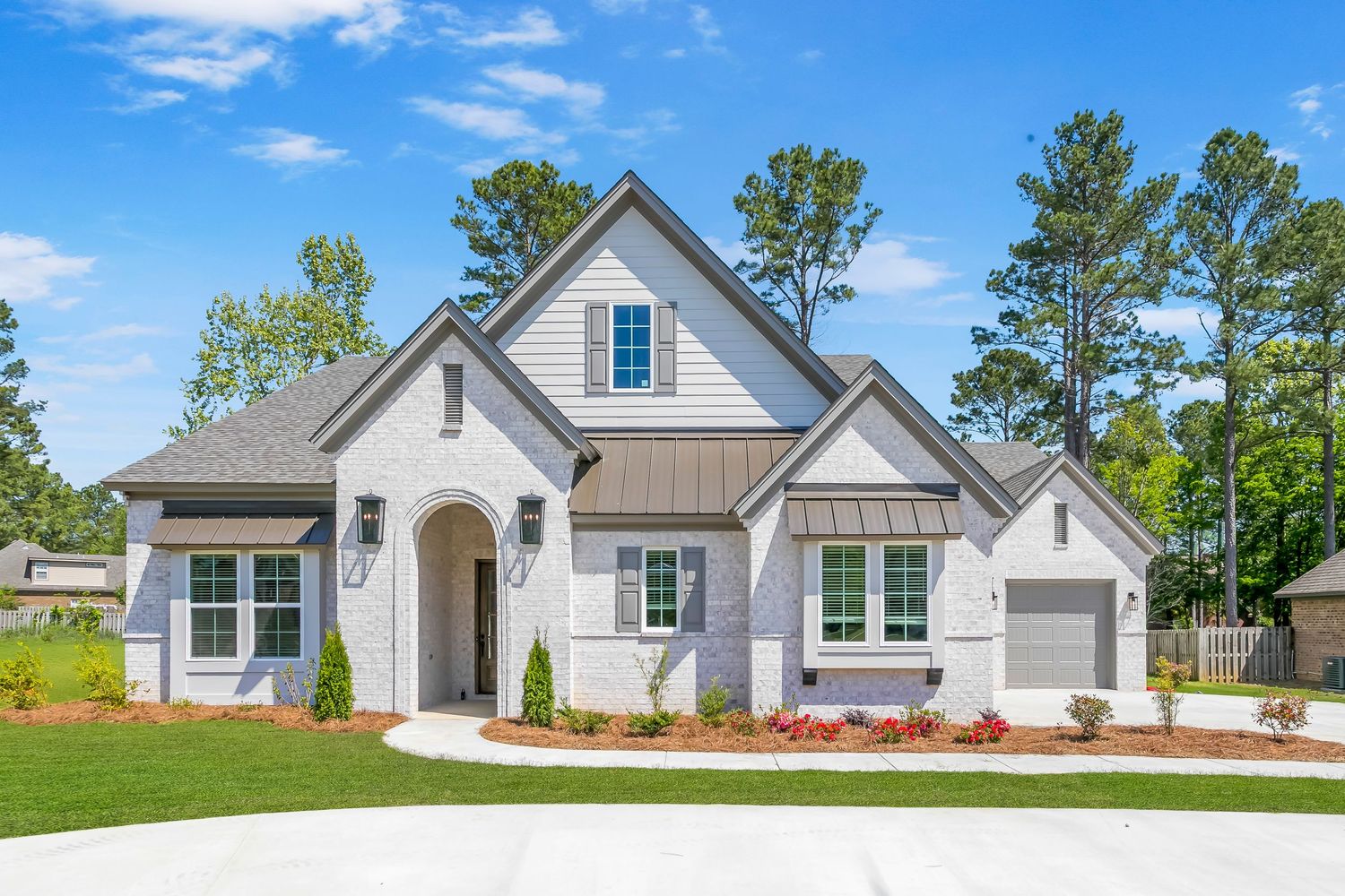 Beautiful modern craftsman style home with gray stucco exterior, arched entryway and attached garage on manicured lawn.