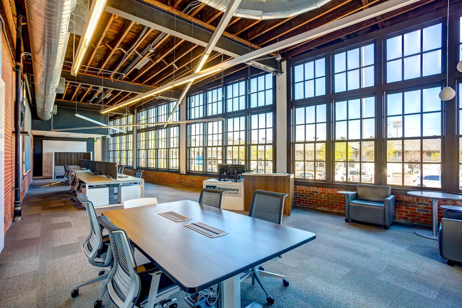 Modern office conference room with large windows, exposed wooden beams, and contemporary furniture in an industrial space.