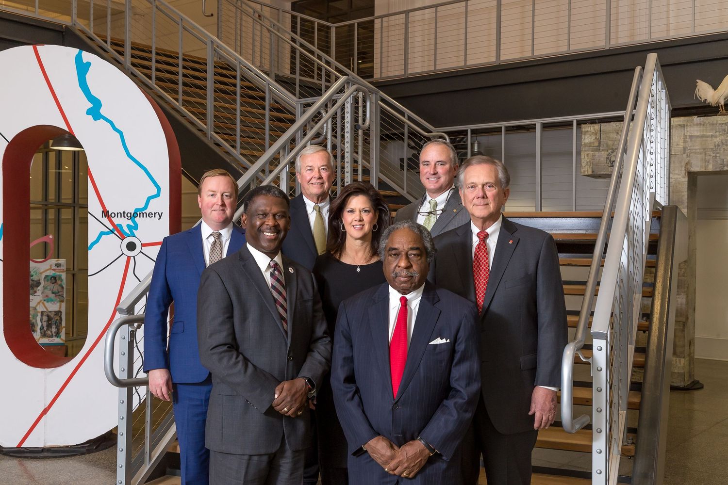 Group of business professionals standing together in an office building lobby near a modern staircase.