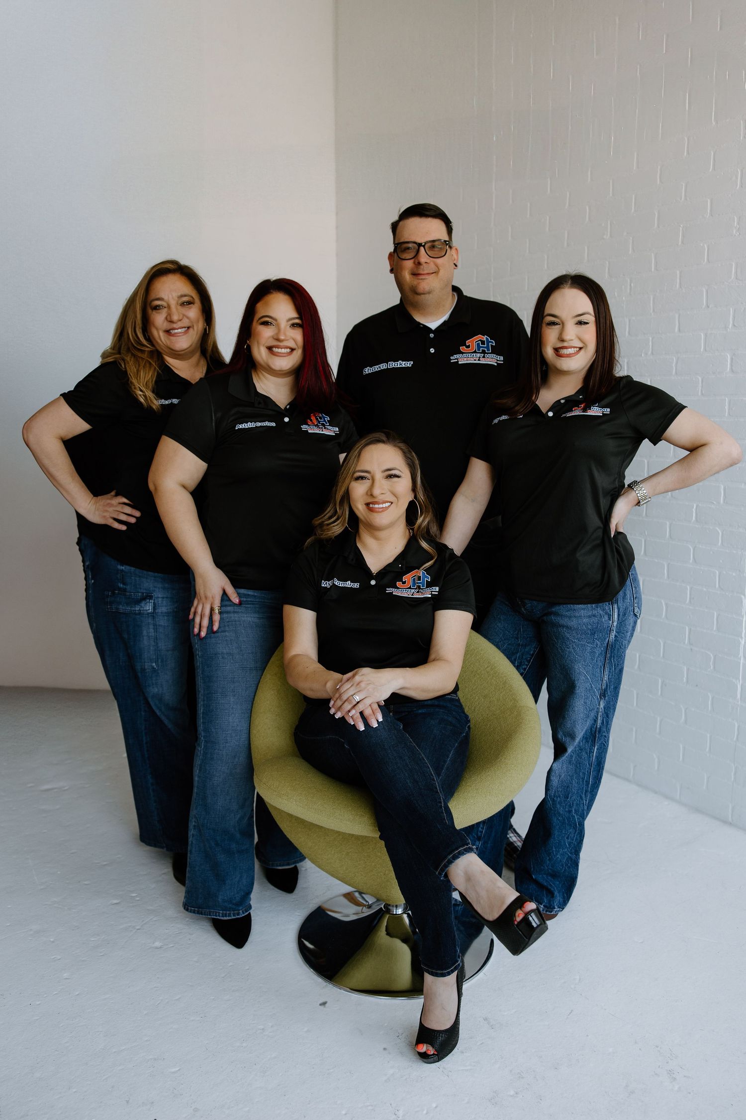 Business team wearing matching black polo shirts poses together with one member seated in yellow chair.