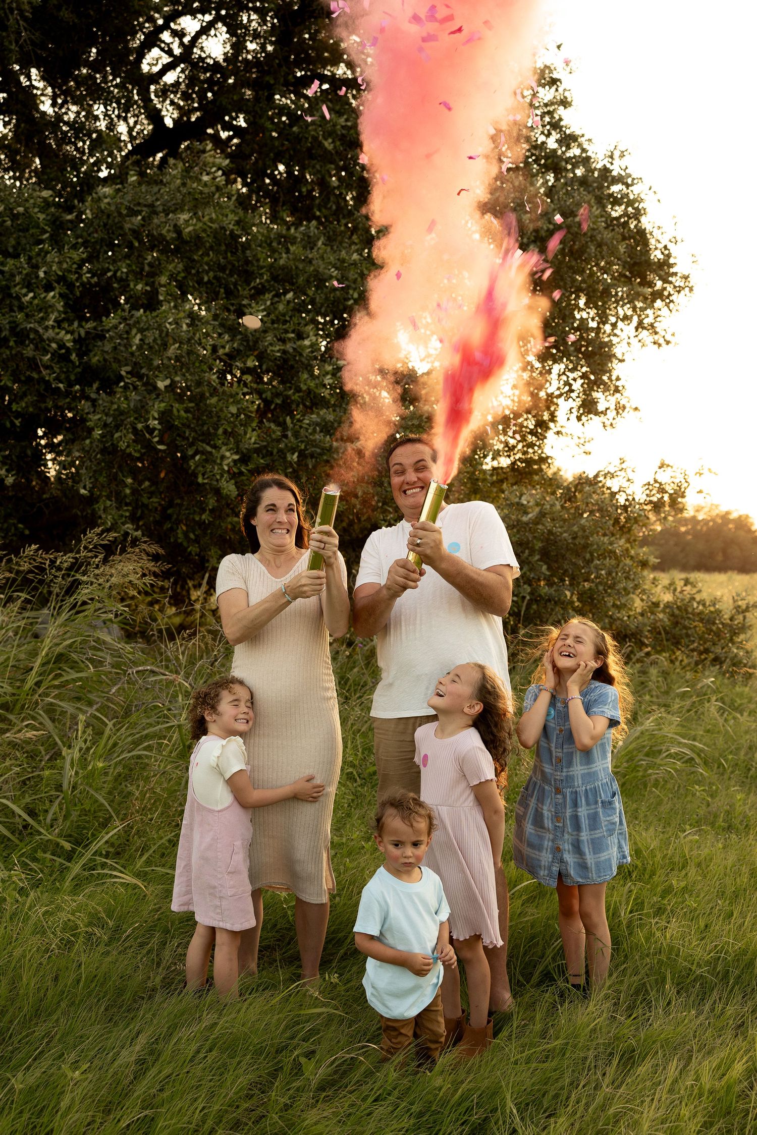 Family gathering at sunset with pink smoke flares in grassy field.