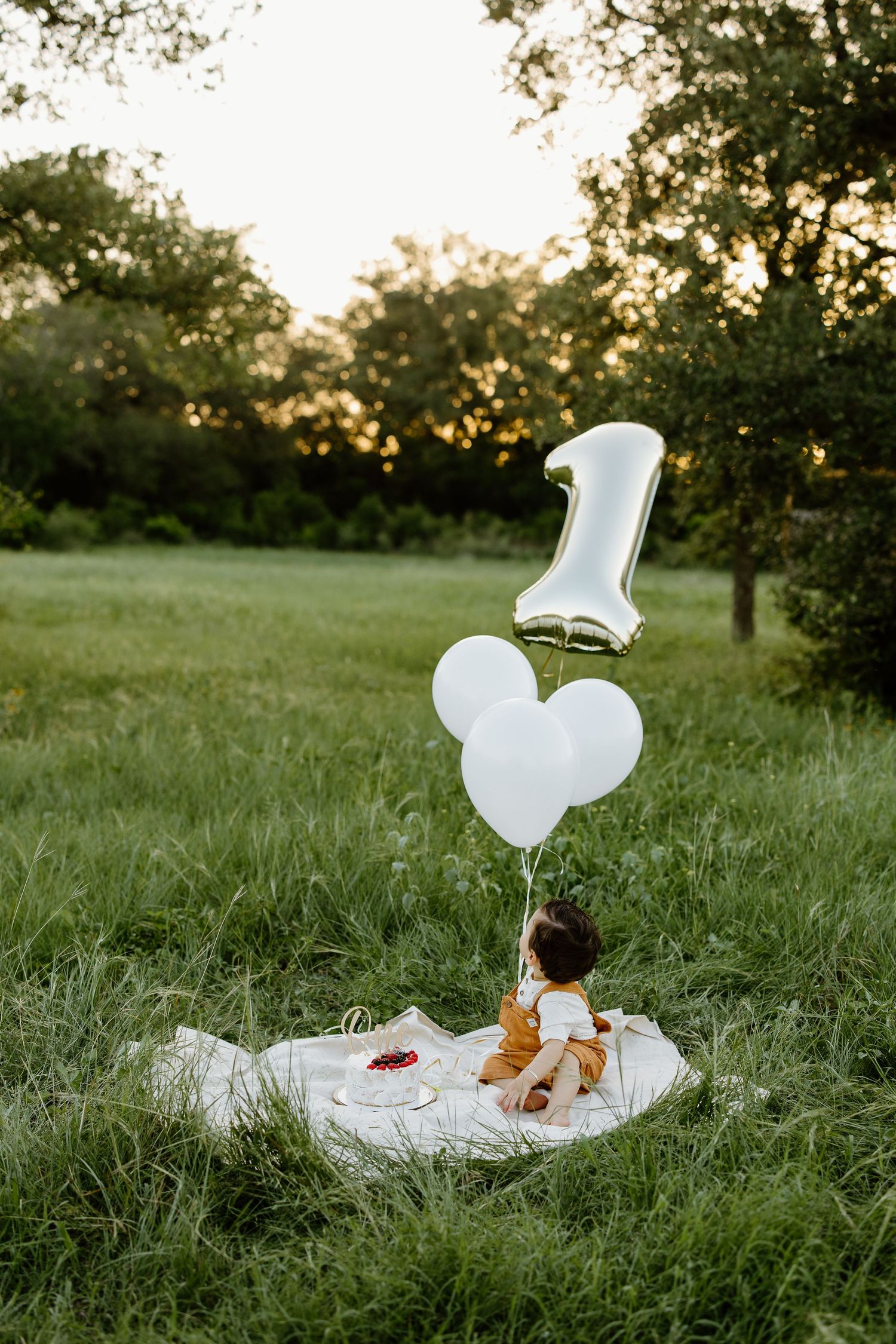 White heart balloons float beside picnic setup in grassy field at sunset.