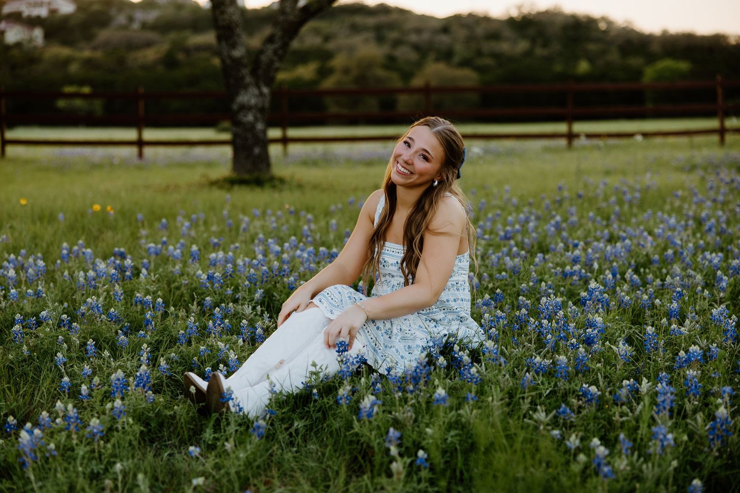 Person sitting in field of blooming bluebonnets wearing white dress during spring photo session.