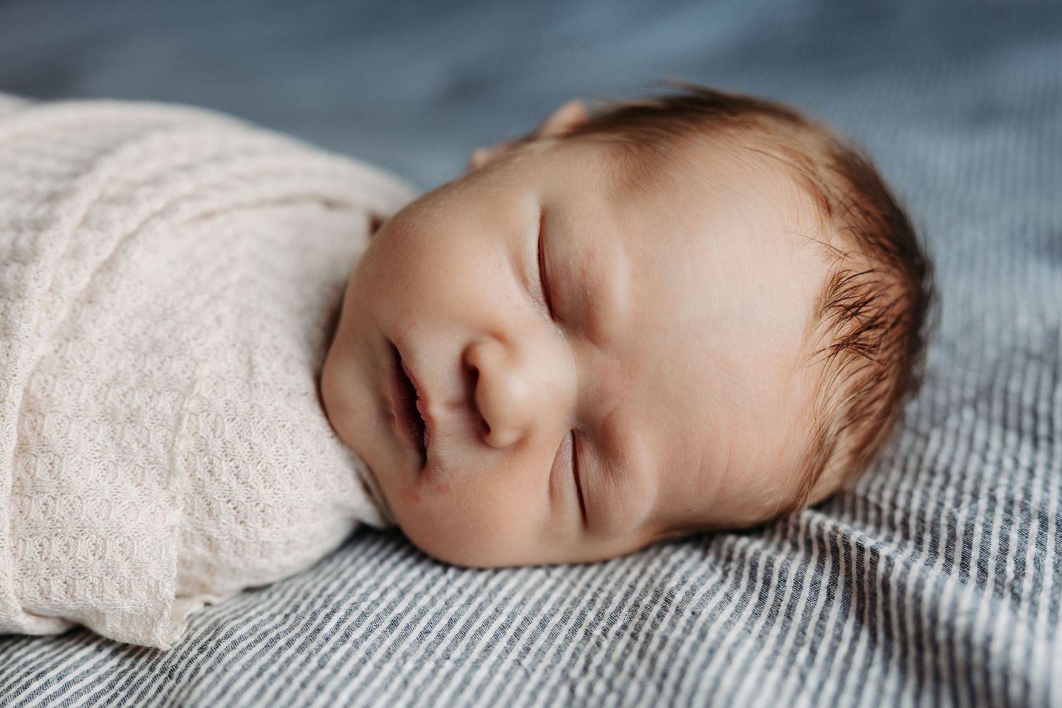 Sleeping baby peacefully rests on soft gray textured blanket in natural light.