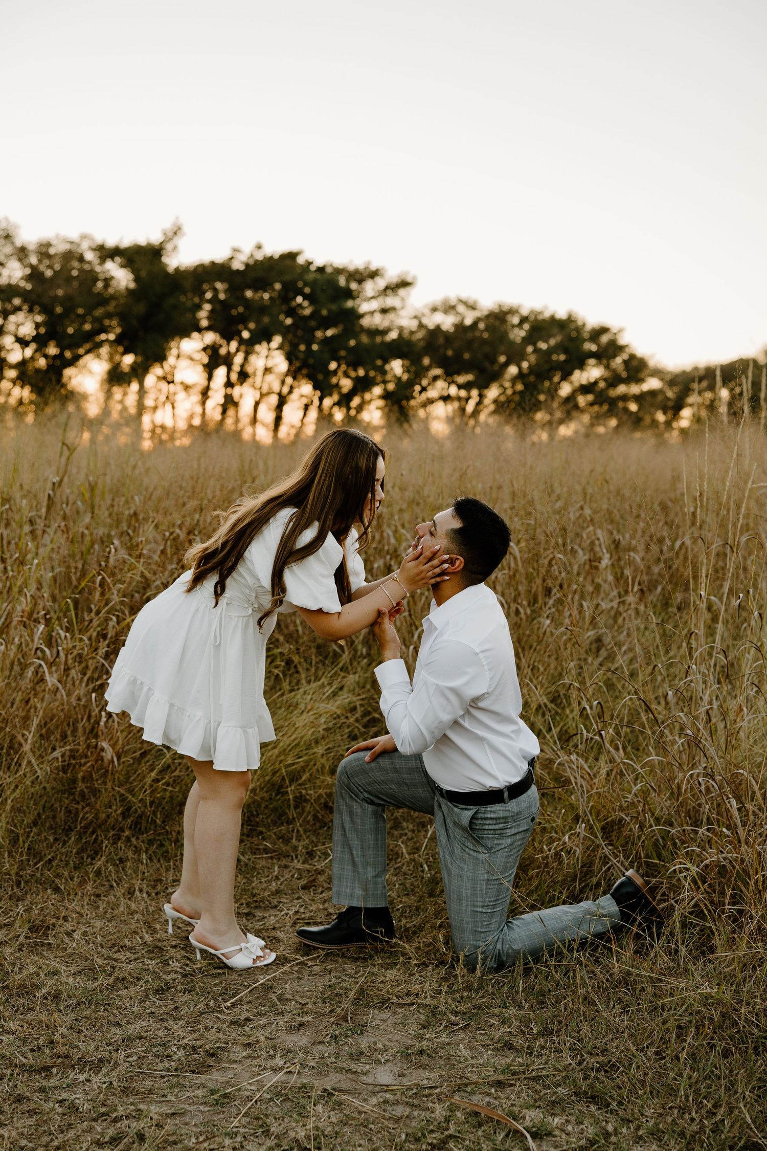 Happy couple sharing emotional moment during surprise proposal in field at sunset.