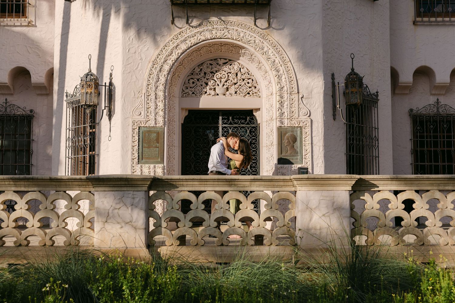 Couple embracing under ornate Moorish arch on decorative stone balcony of historic white building.