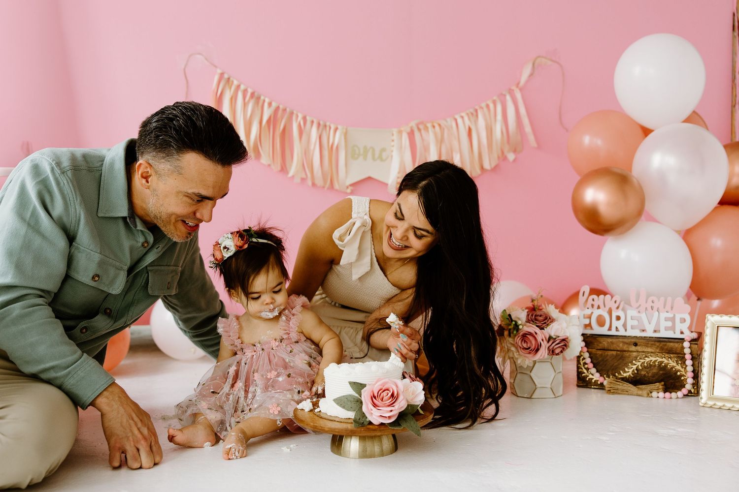 Family celebrating a first birthday party with pink and gold decorations.