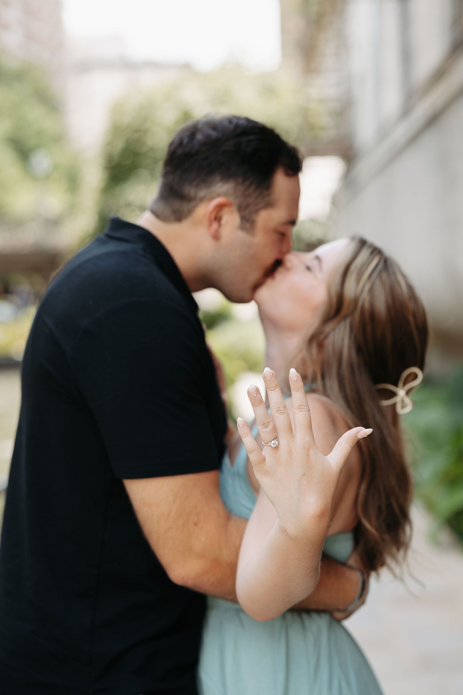 A romantic engagement photo shows a couple kissing while the woman displays her new ring.