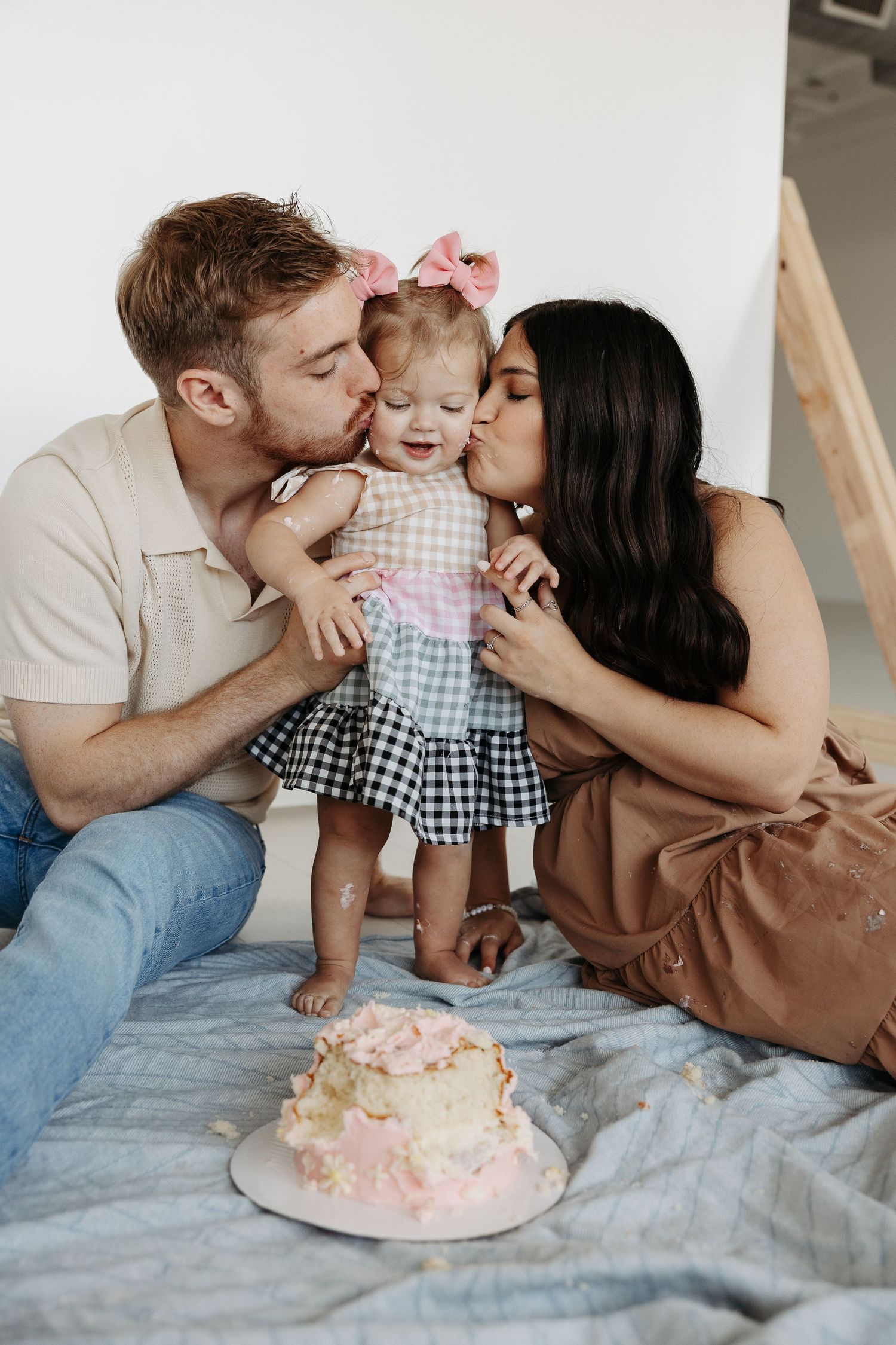 A series of five photos showing a family having fun with a cake smash photoshoot on a bed.