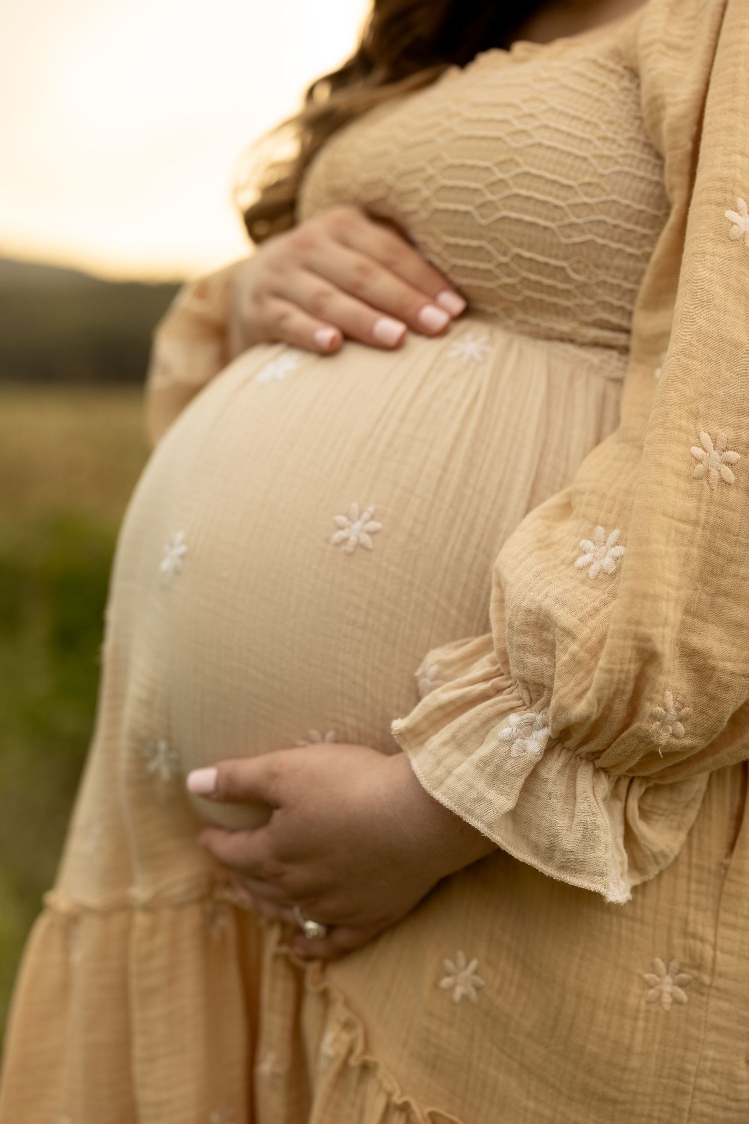 Close-up series of pregnant belly in beige embroidered dress during maternity photoshoot.