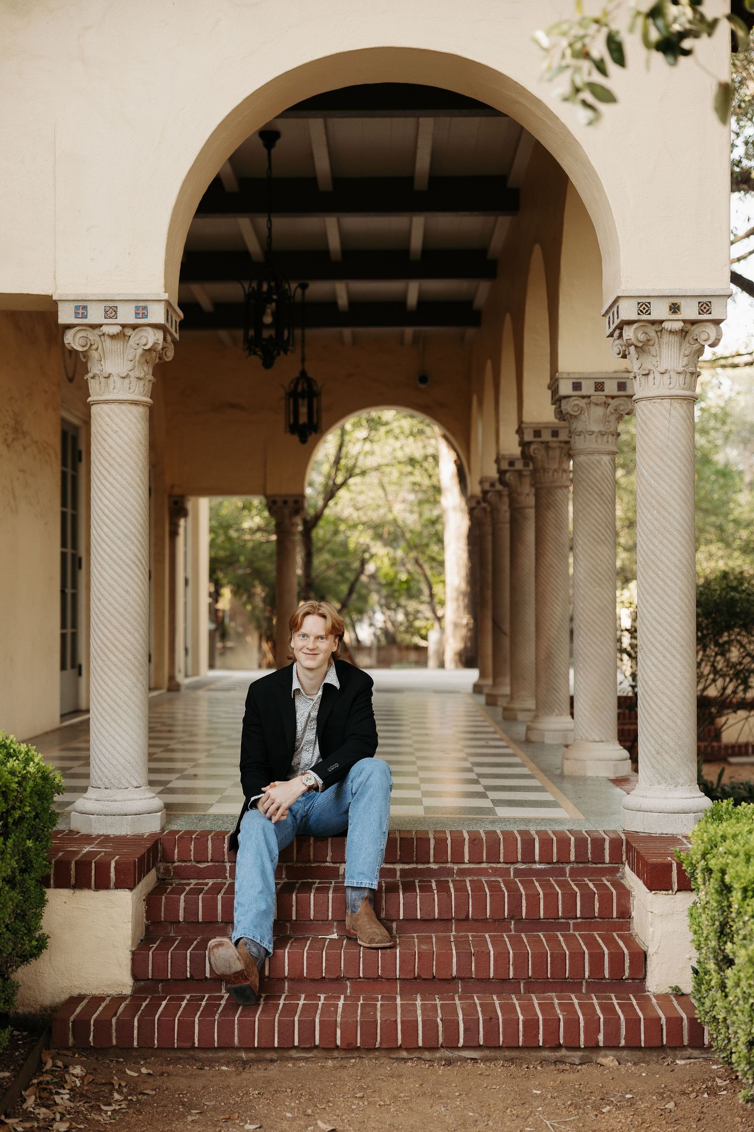 Person sitting on brick steps under elegant arched colonnade during portrait photography.