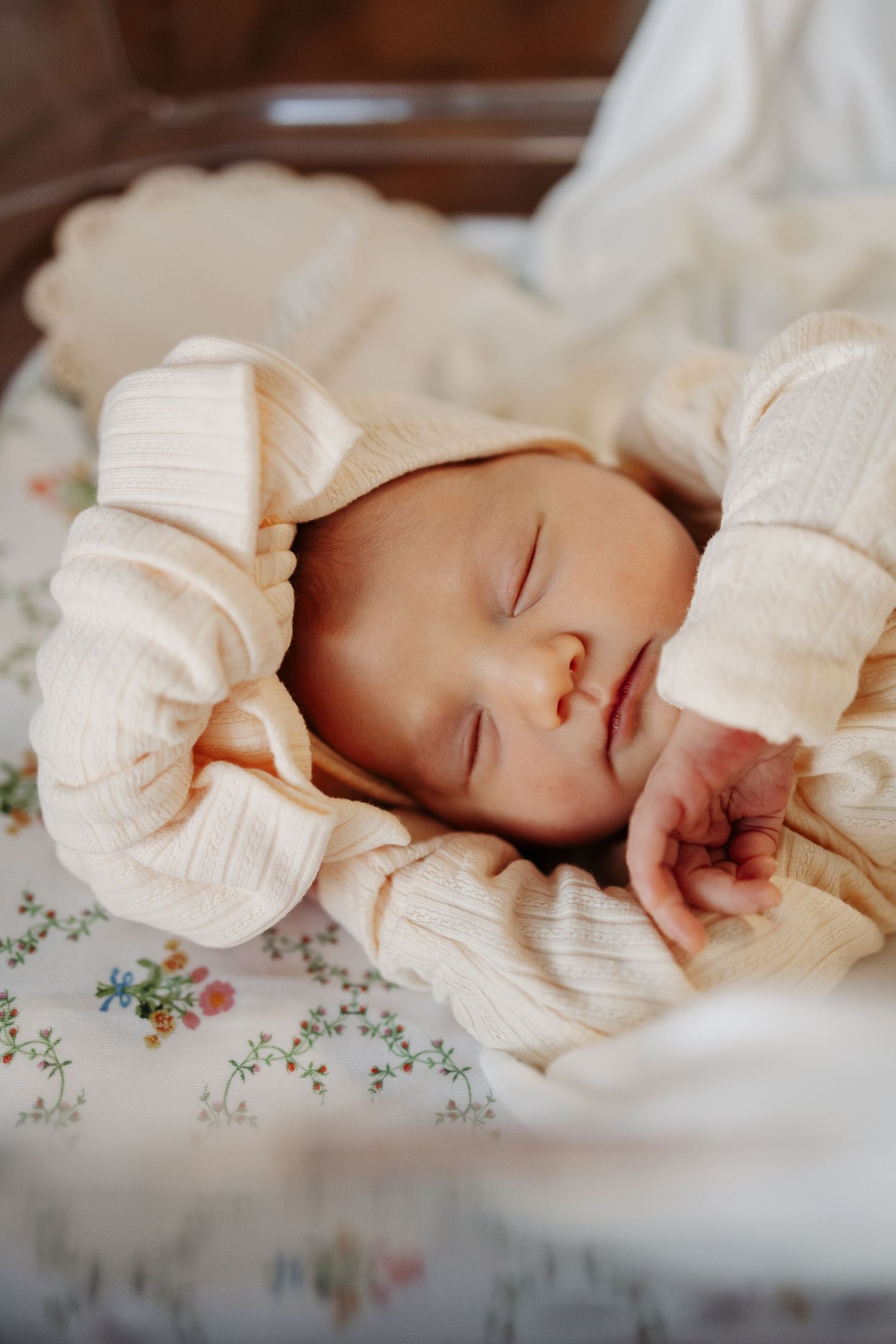 A sleeping baby in white clothing rests peacefully on floral patterned bedding.