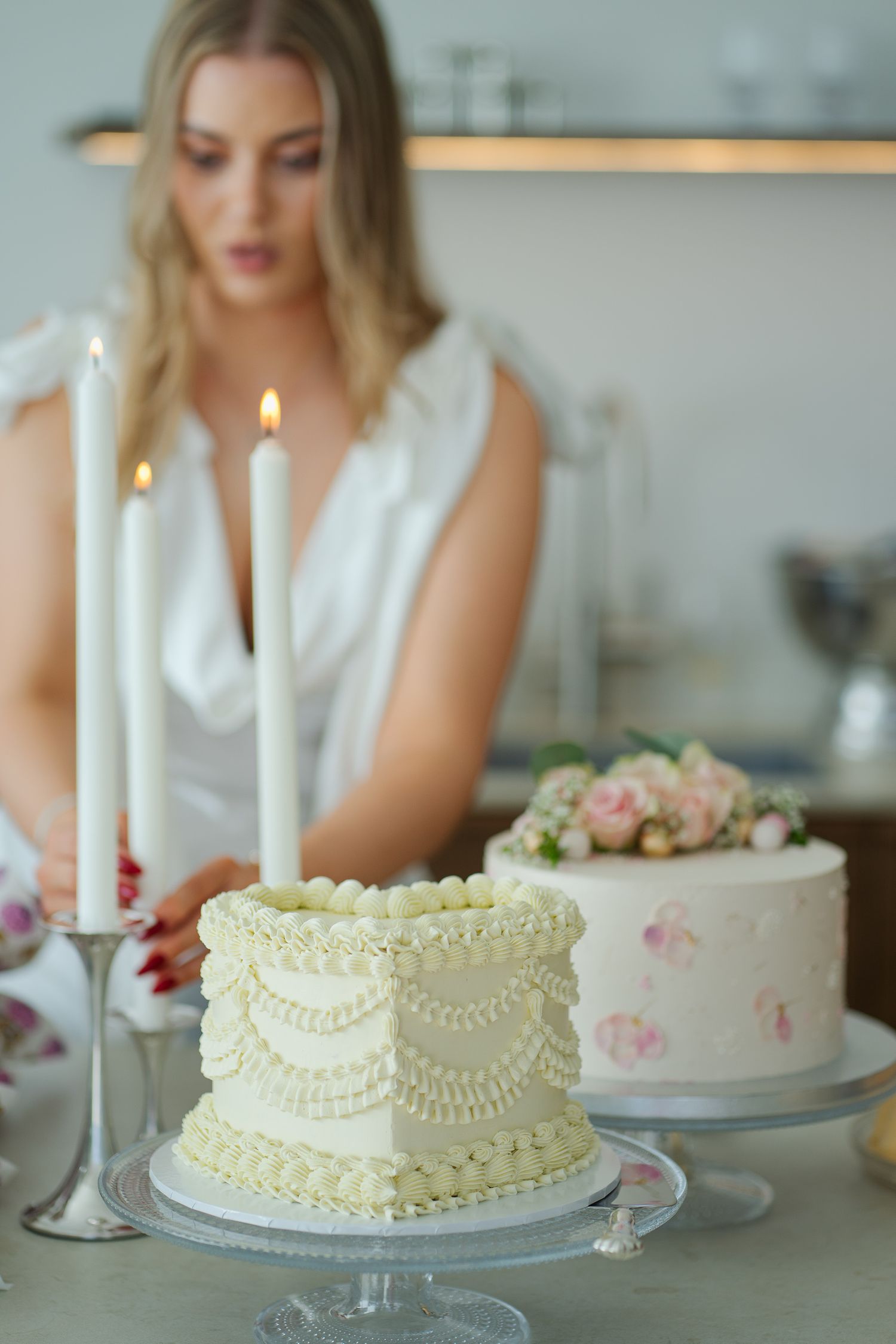 Elegant white and pink wedding cakes with lit candles on display.