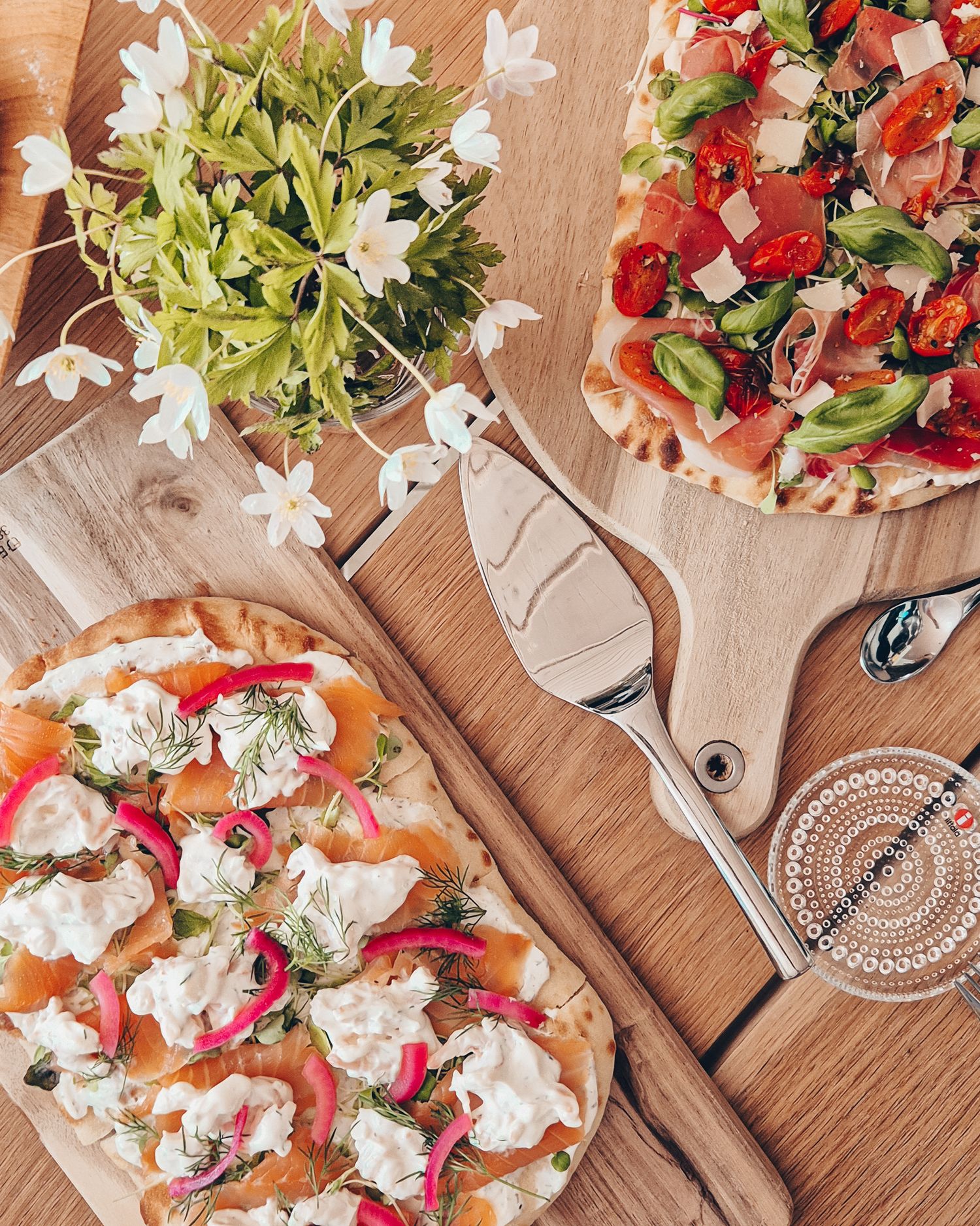 Rustic flatbread pizza topped with fresh strawberries, ricotta, and white flowers served on wooden board.