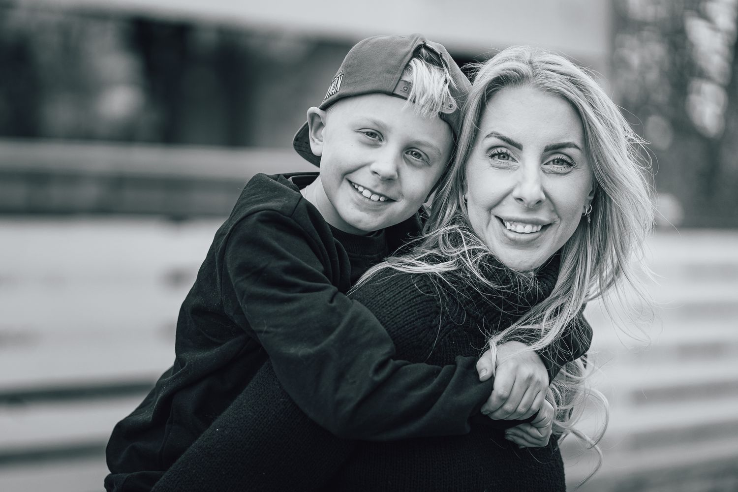 Black and white portrait of a mother and young child sharing a joyful embrace outdoors.