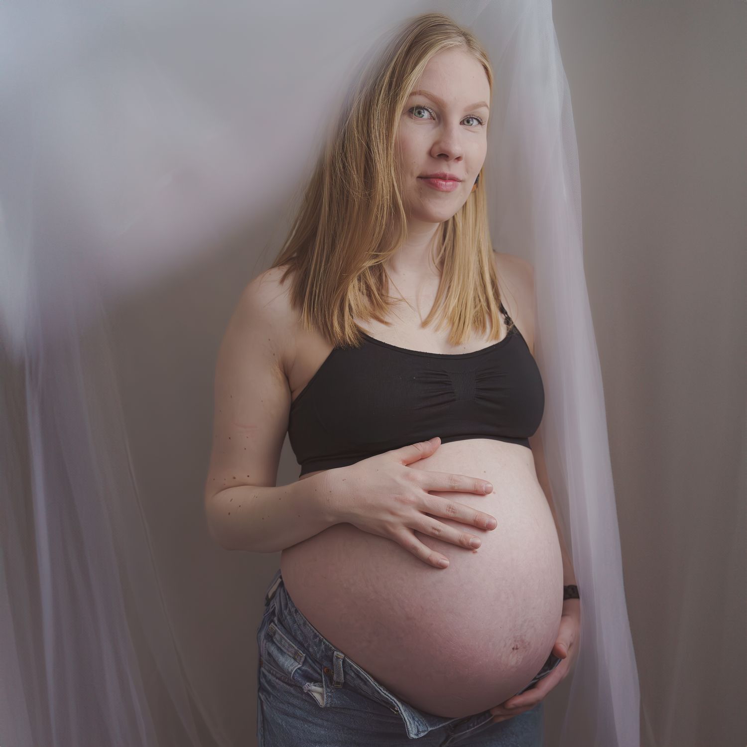 Side view of pregnant woman in black top showing her baby bump against white backdrop.