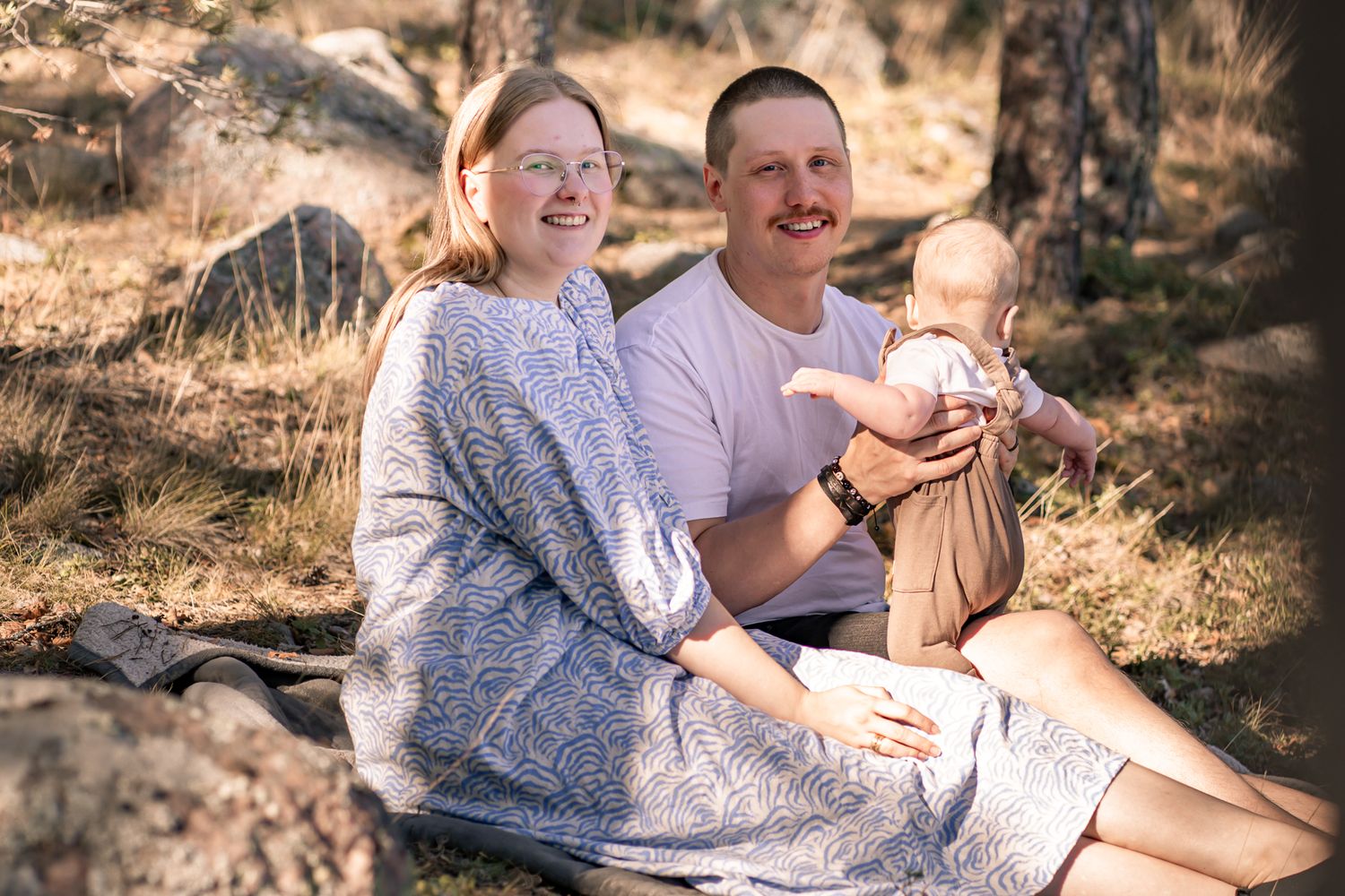 Family sitting together outdoors on rocks during a sunny autumn day.