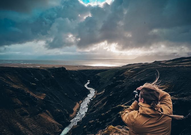 Photographer captures dramatic landscape with winding river and moody sky from cliff edge.