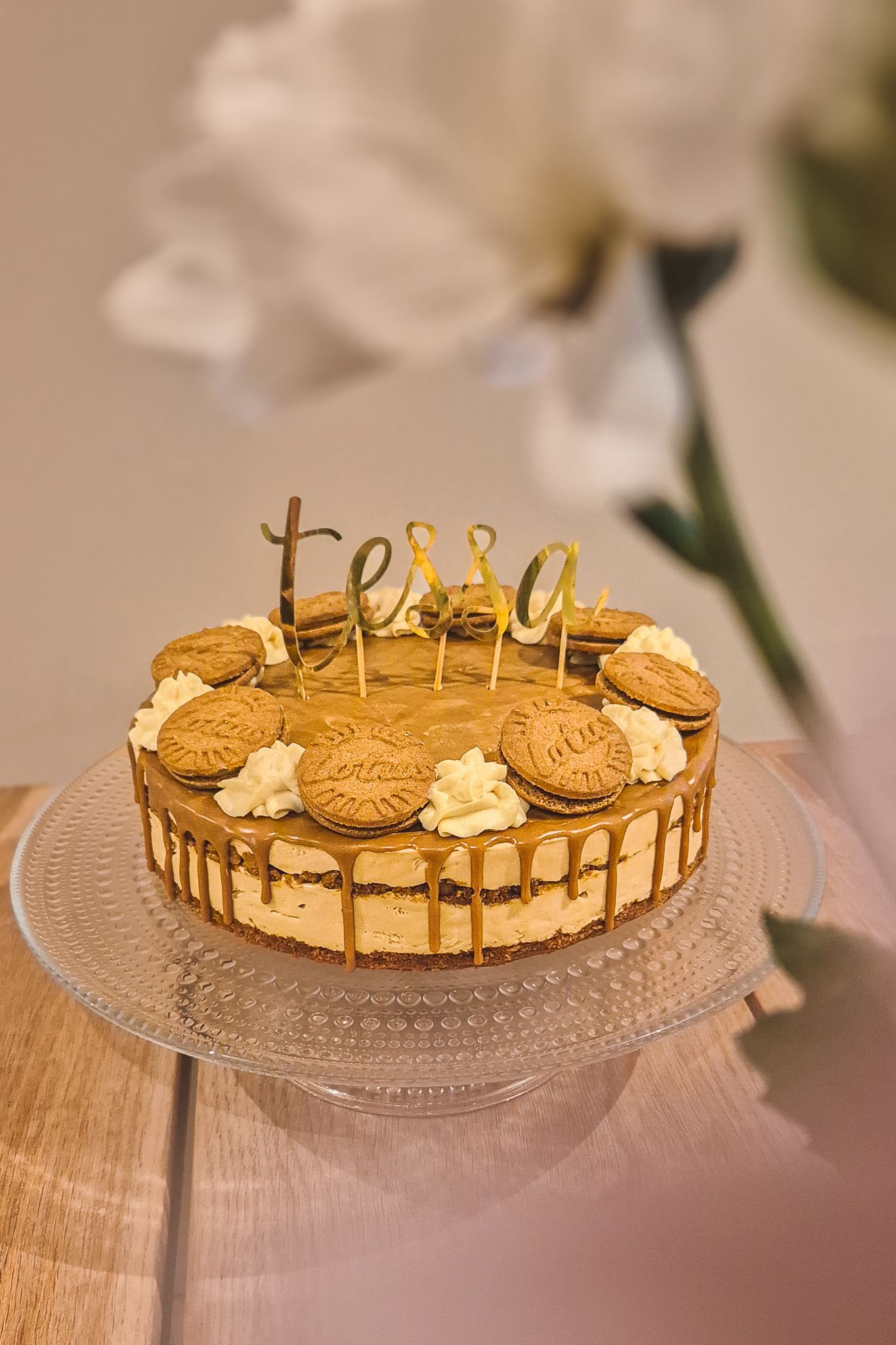 Golden drip cake decorated with cookies and gold 'tessa' text topper.