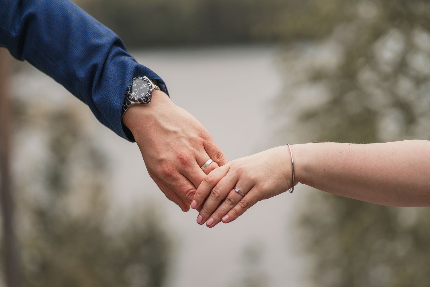 Two people reach out to hold hands together in a tender moment against a soft blurred background.