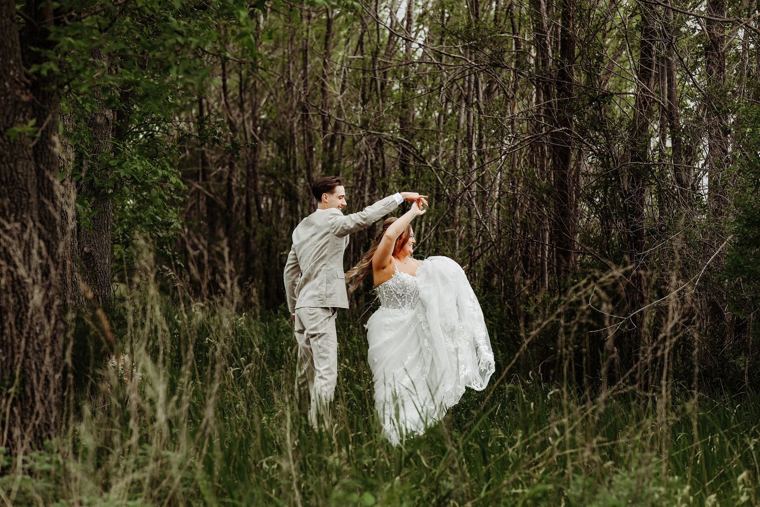 A person in a flowing white dress moves gracefully through a wooded forest setting during a photoshoot.