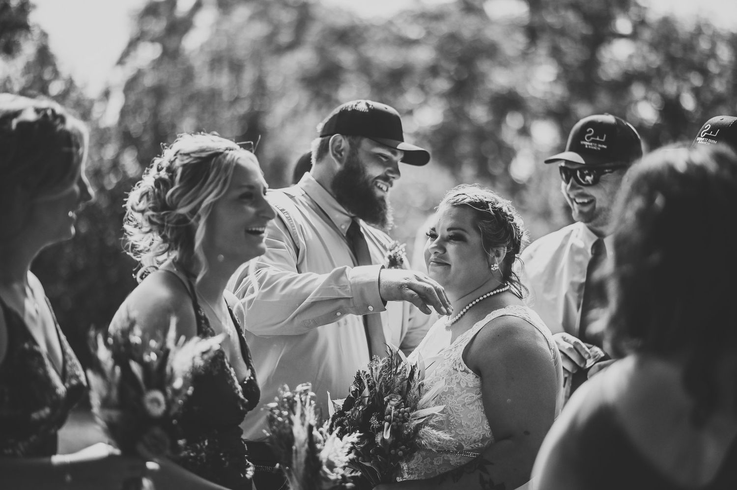 Black and white candid wedding photo showing emotions and interactions during an outdoor celebration with flowers.