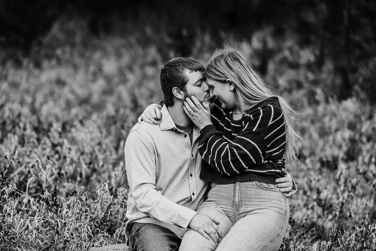 A couple shares a romantic moment together while lying in a grassy field, captured in black and white photography.