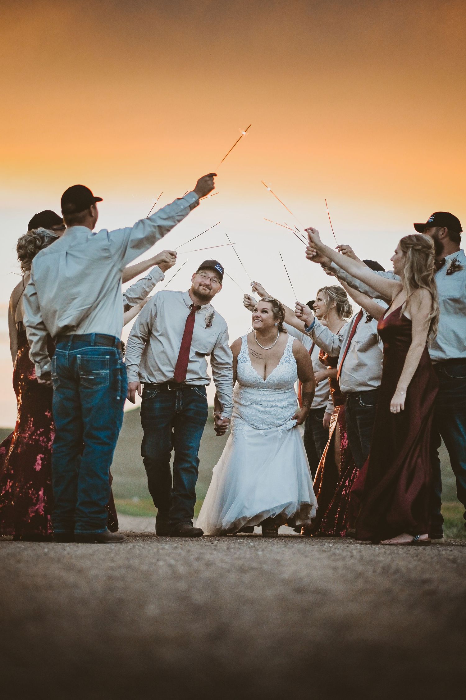 Wedding party members raise sparklers in a joyful celebration at sunset during an outdoor wedding ceremony.