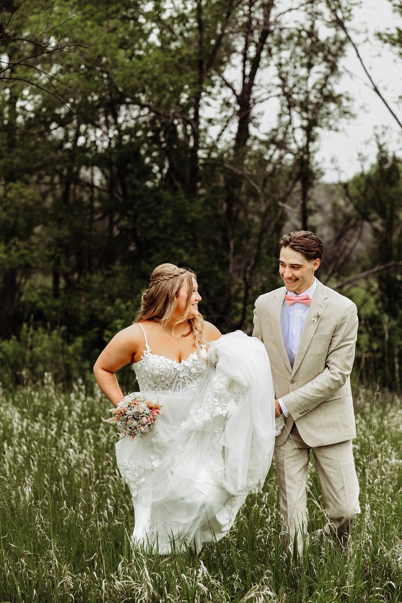 A wedding couple stands together in a meadow of tall grass, sharing a joyful moment on their special day.
