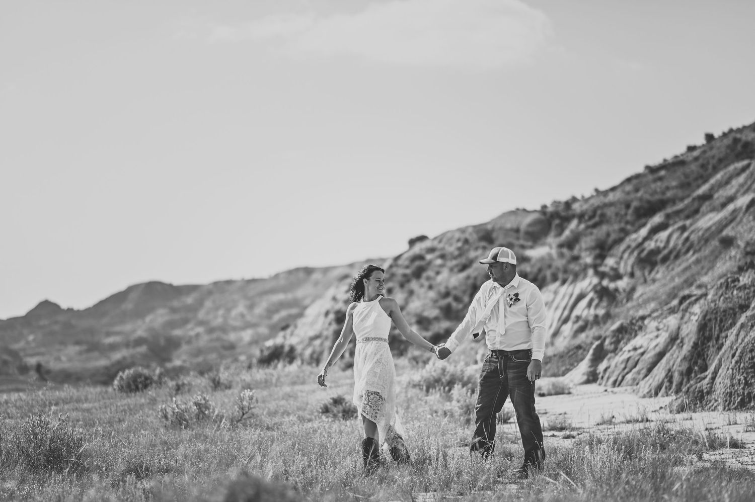 A wedding couple walking hand in hand along a scenic hillside trail in black and white.
