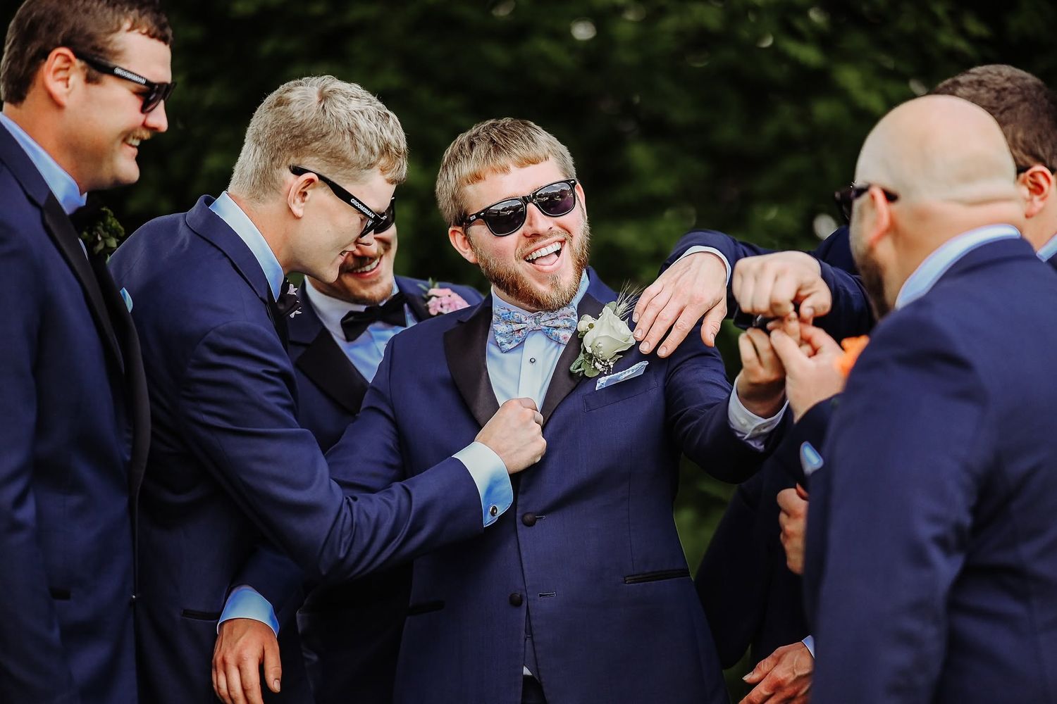 Groomsmen in navy suits share laughter and candid moments during outdoor wedding photography session.