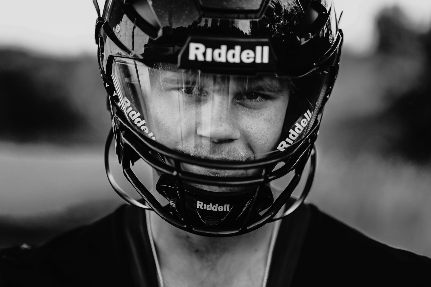 Black and white close-up photo of senior football player wearing a Riddell helmet with protective face mask.