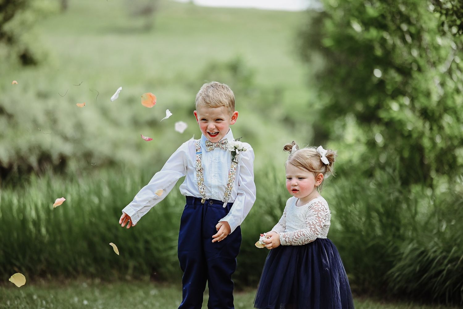 Two small children walk and play outdoors in classic clothing while colorful fall leaves float around them.