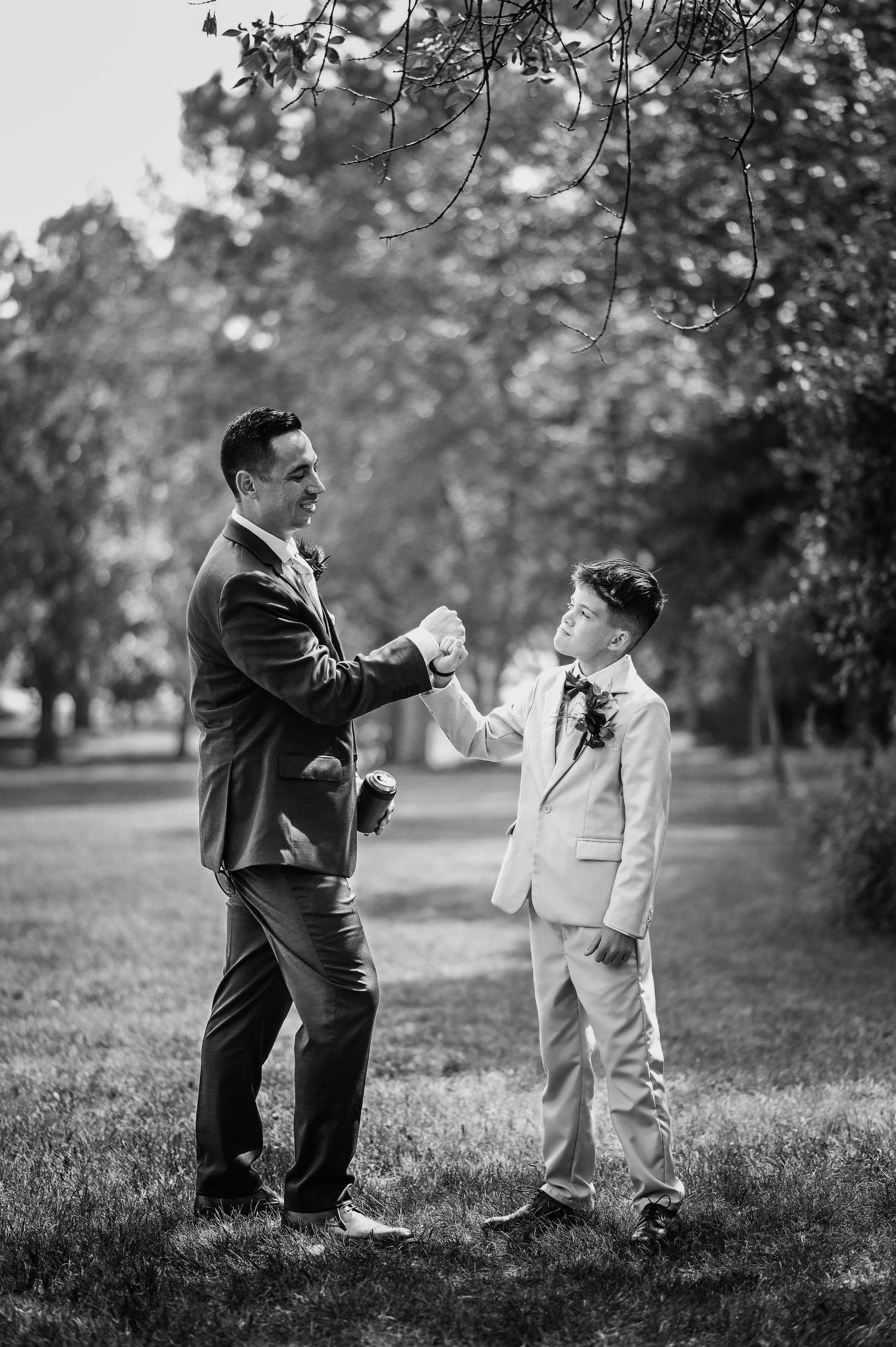 Black and white photo of a tender moment between a groom and child in formal attire outdoors.