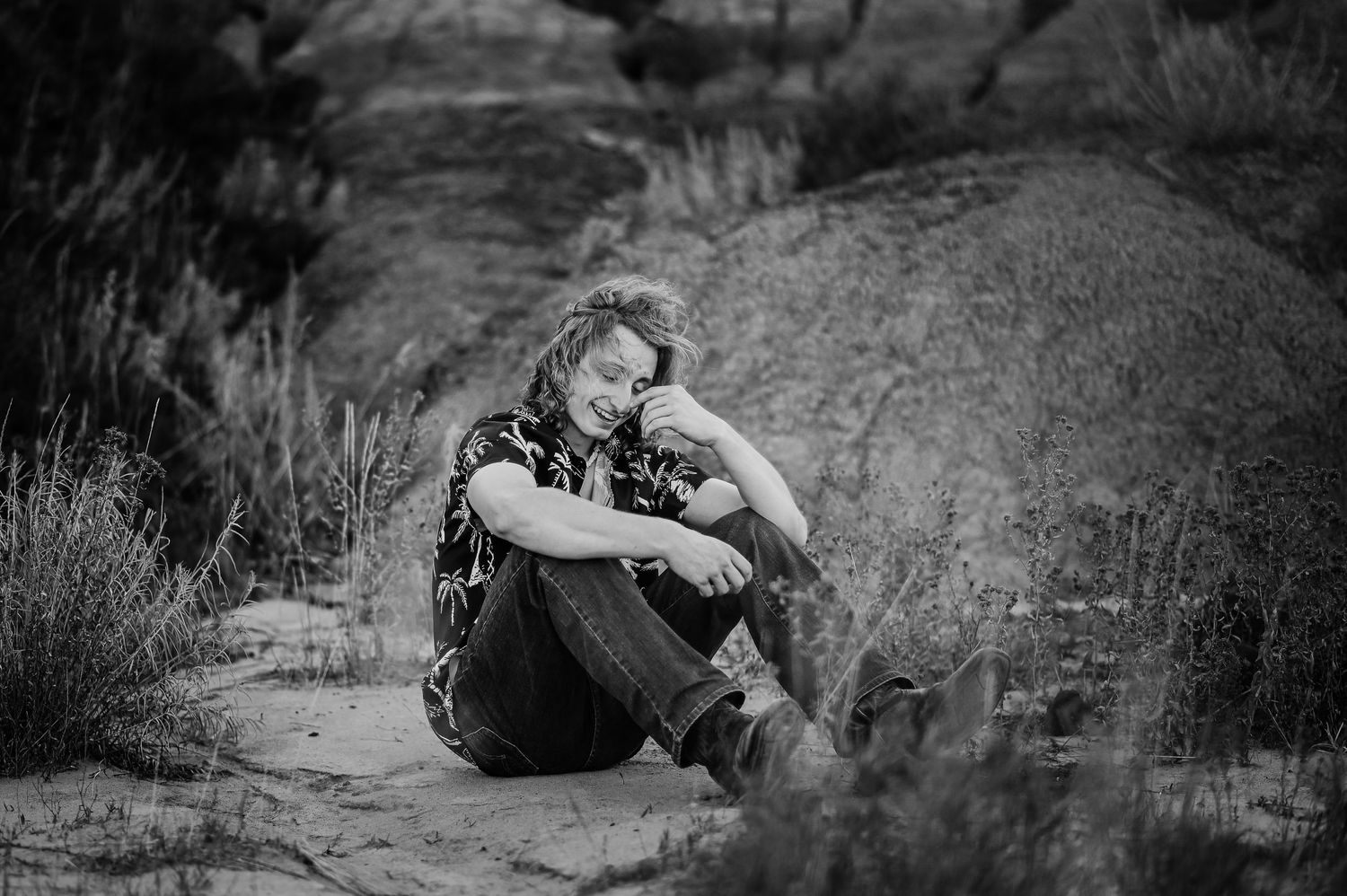 Black and white portrait photograph of a senior boy sitting on a rock in an outdoor desert landscape.
