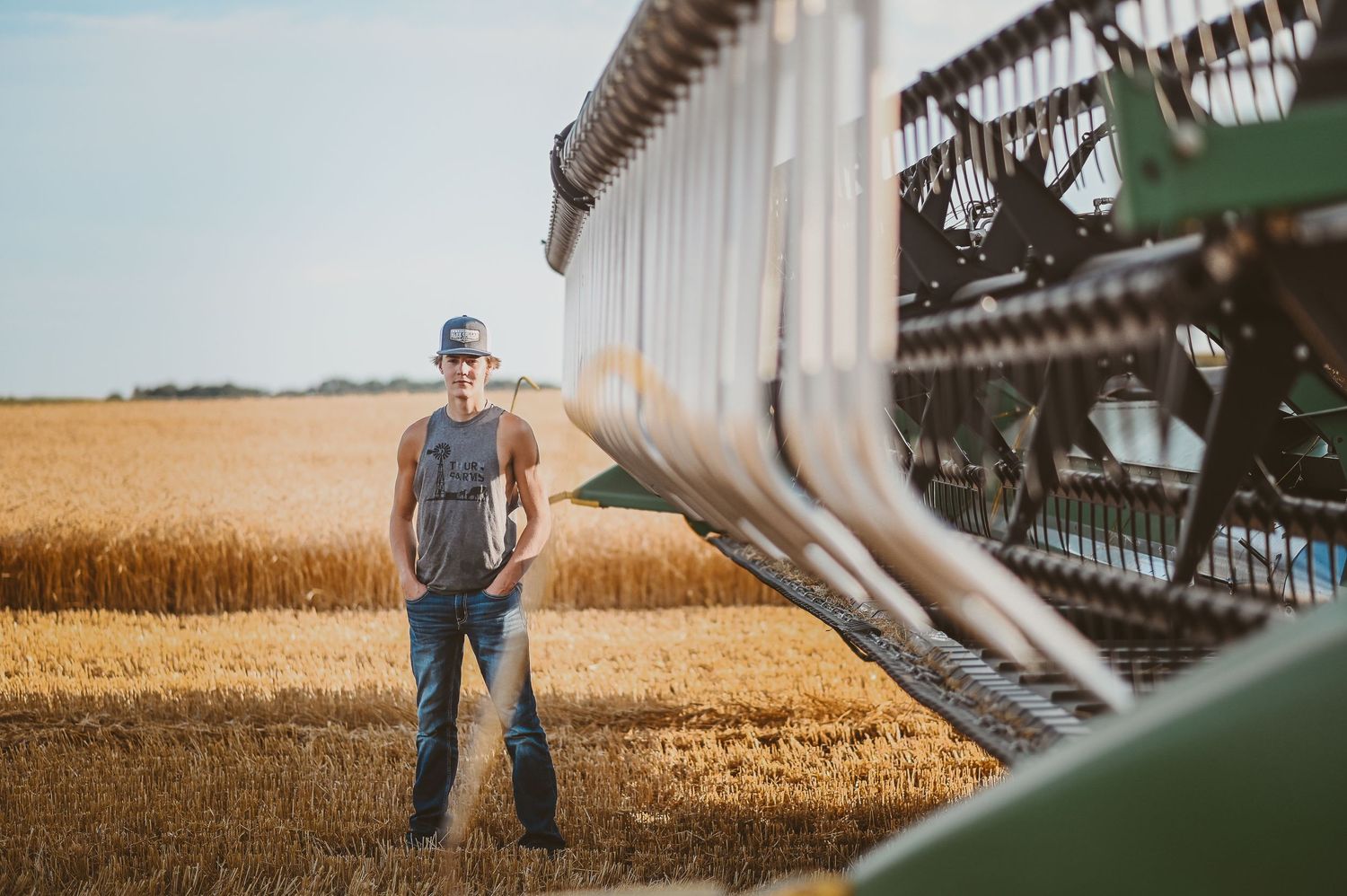 Farmer standing in a golden wheat field next to a combine harvester during harvest season.