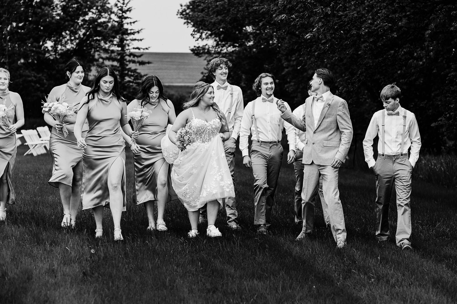 A vintage black and white photograph showing a group of people walking casually across a grassy lawn near trees.