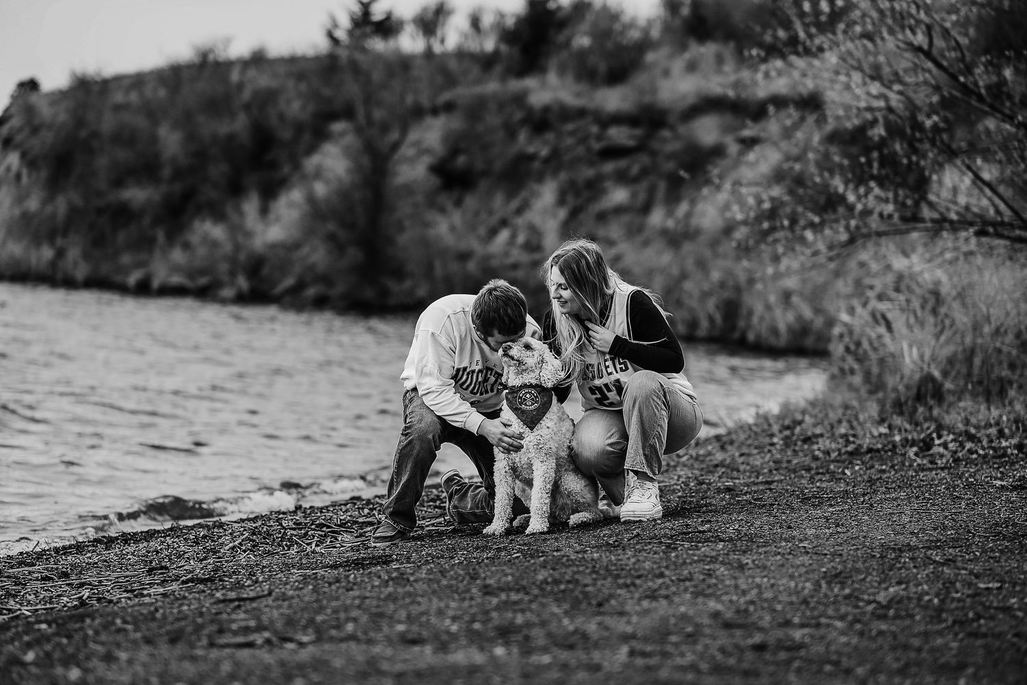 A group sits at the edge of a lake with their golden retriever in this black and white photo.