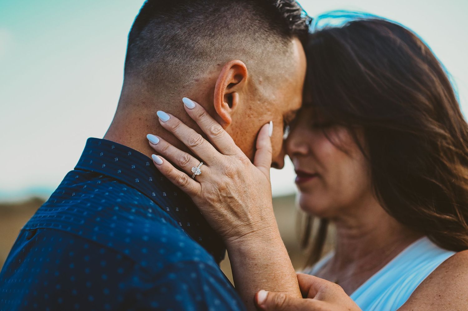 Close-up romantic couple embracing in tender moments against blue sky background.