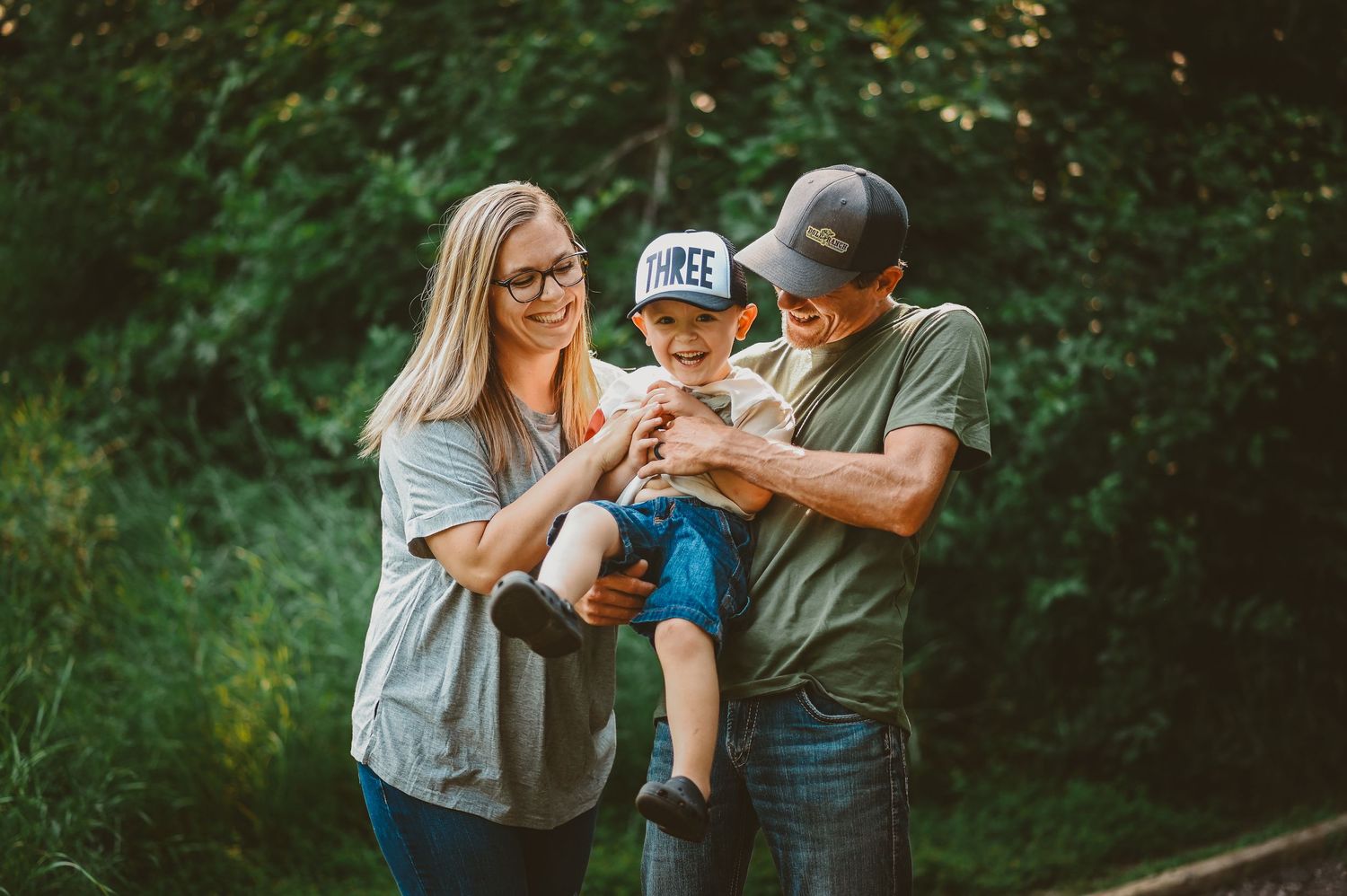 A young couple holds their toddler son between them while spending time outdoors on a sunny afternoon.