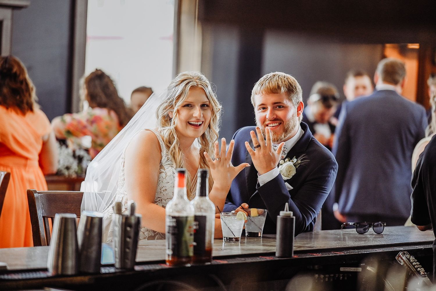 A bride and groom share a moment together at the reception bar surrounded by wine bottles.