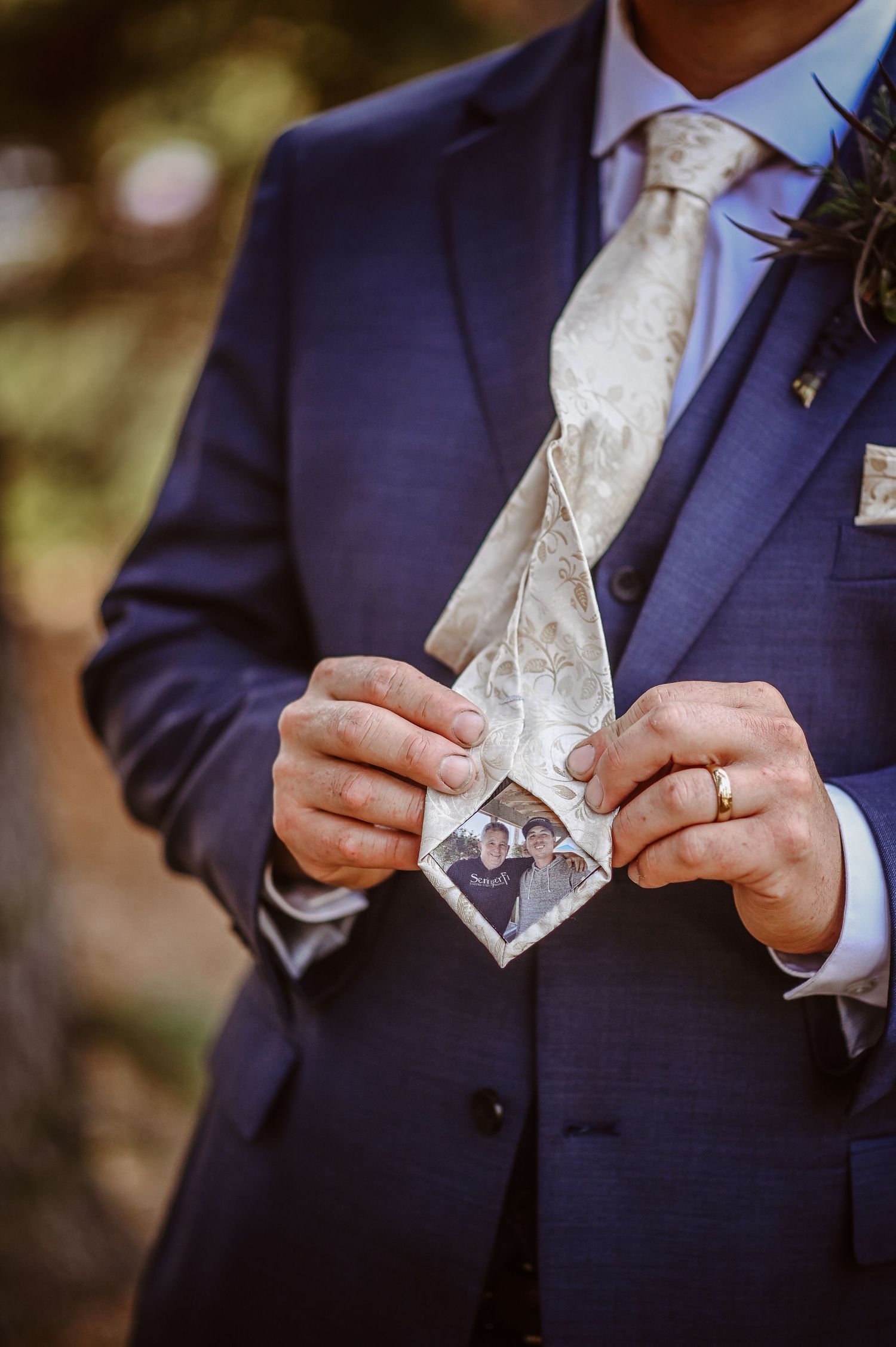 Close-up of hands holding a white patterned necktie with a small photo displayed inside during a formal wedding event.