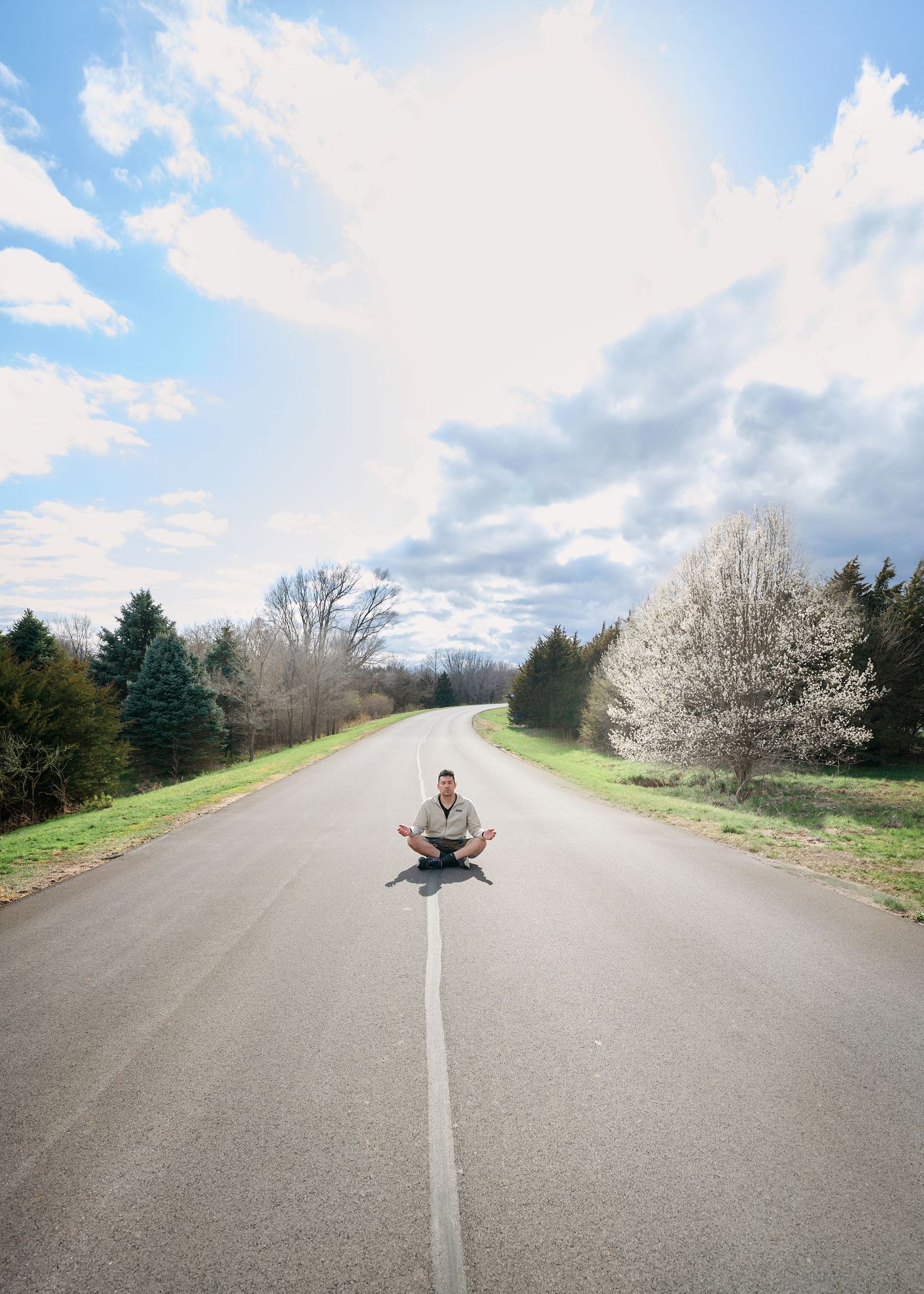 A peaceful scene with someone meditating on an empty country road lined with spring blossoms.