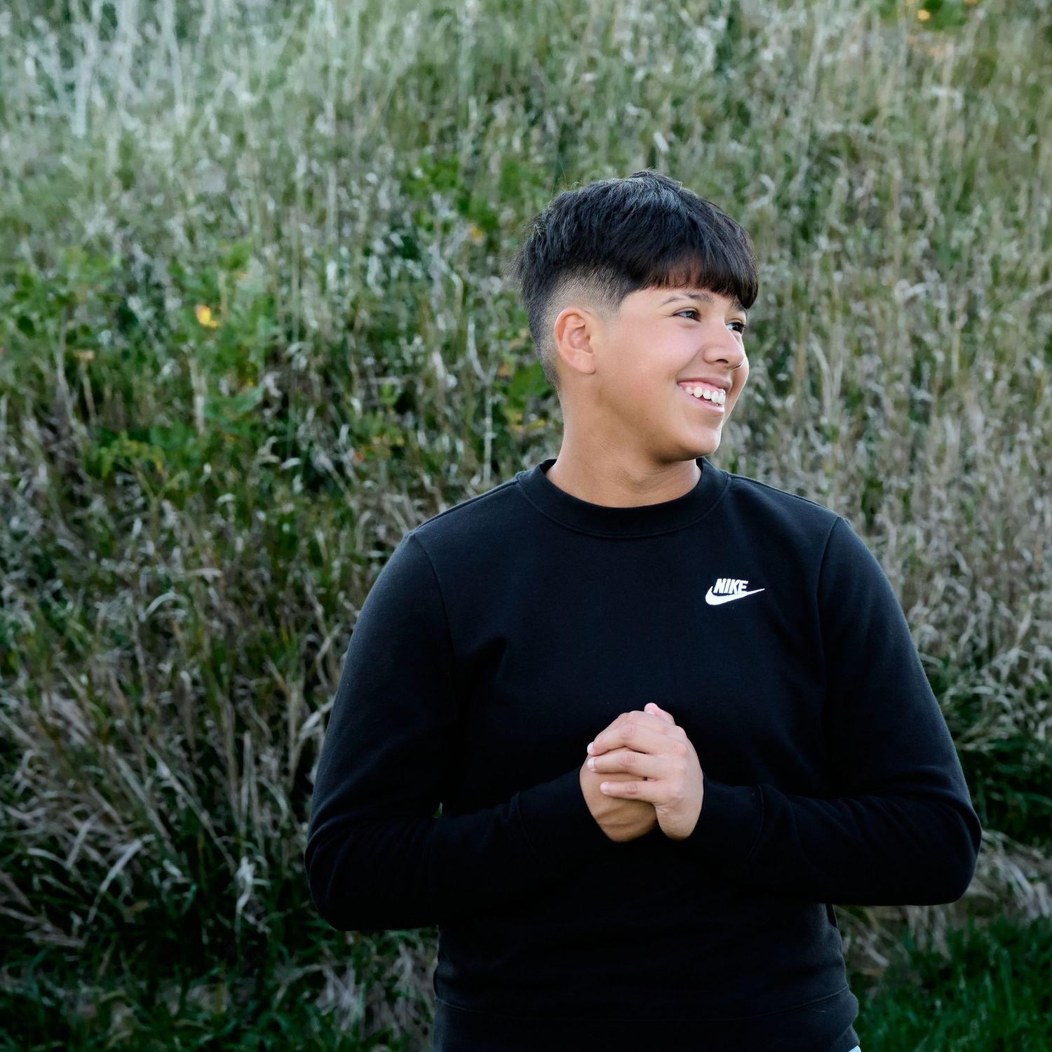 Person in black Nike sweatshirt standing outdoors against natural foliage background.