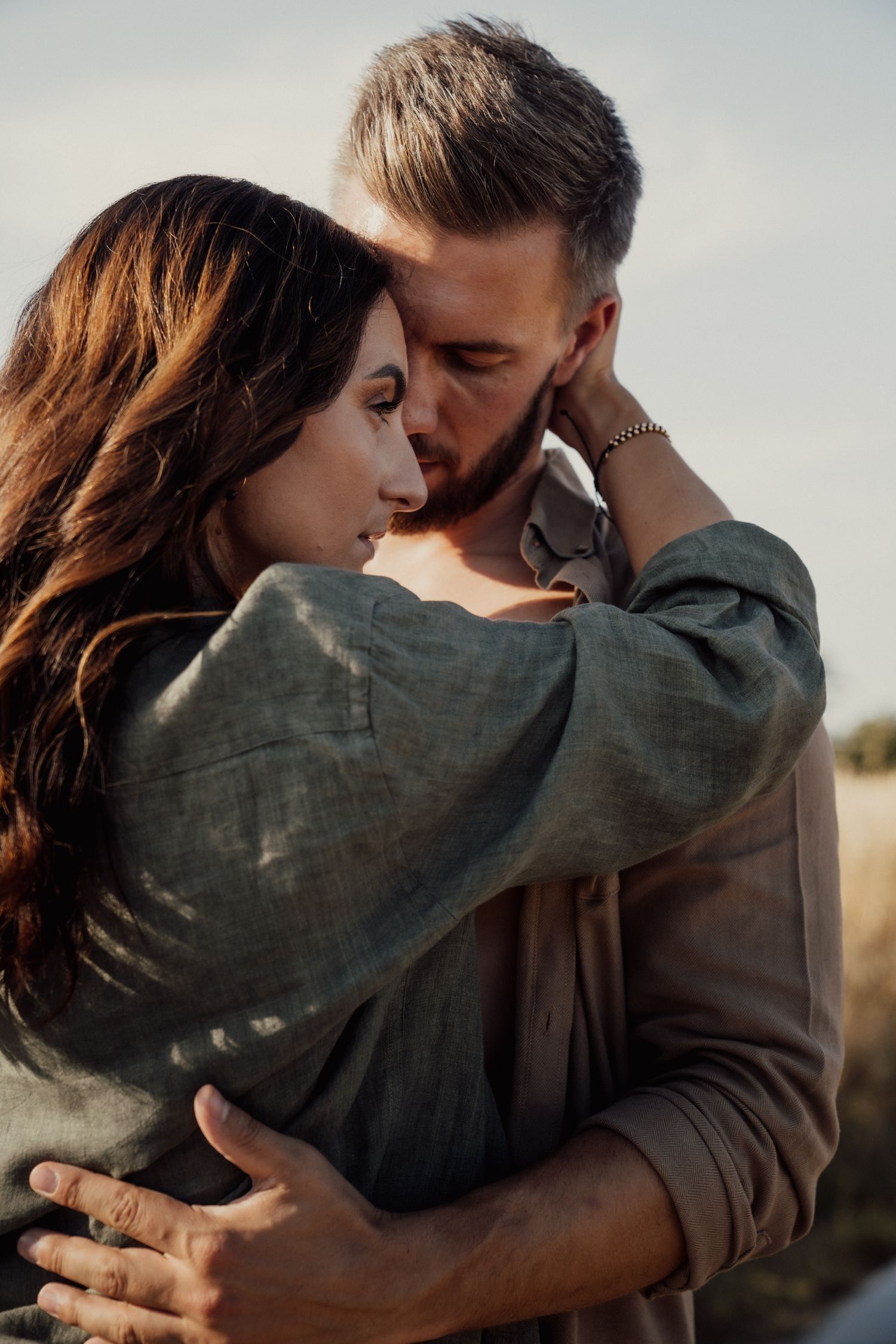 Tender embrace between couple in casual attire against natural outdoor setting.